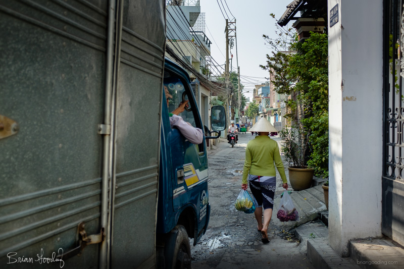 A person in a conical hat walking down a narrow Saigon alley.